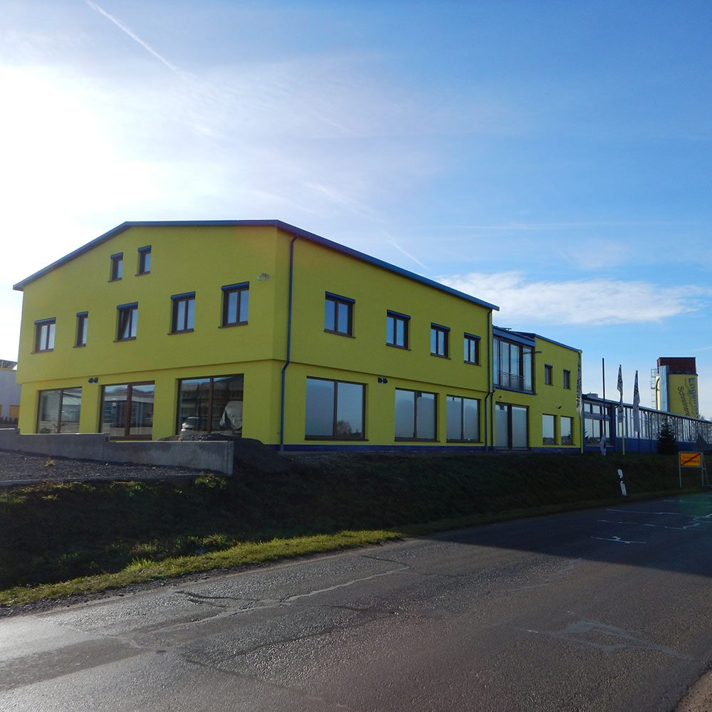 Gelbes zweistöckiges Bürogebäude mit großen Fenstern an einer Straße bei klarem Himmel